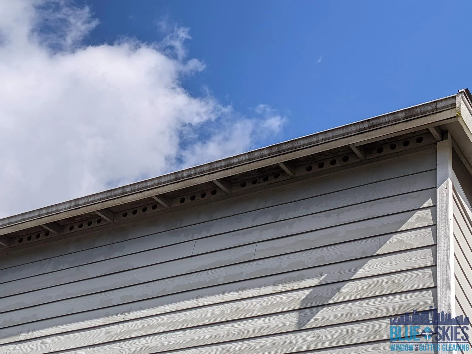 Dirty gutters and siding on a home need cleaning, under a blue sky with white clouds.