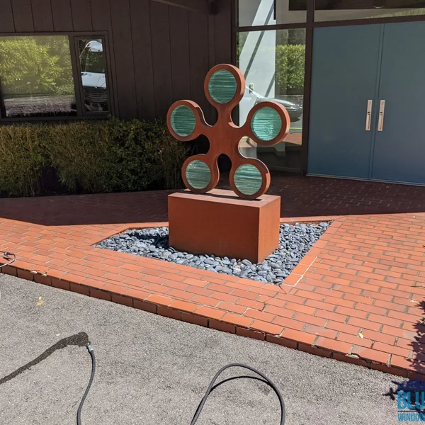 Commercial space entrance with rust-colored sculpture and brick walkway cleaned by our soft wash team.