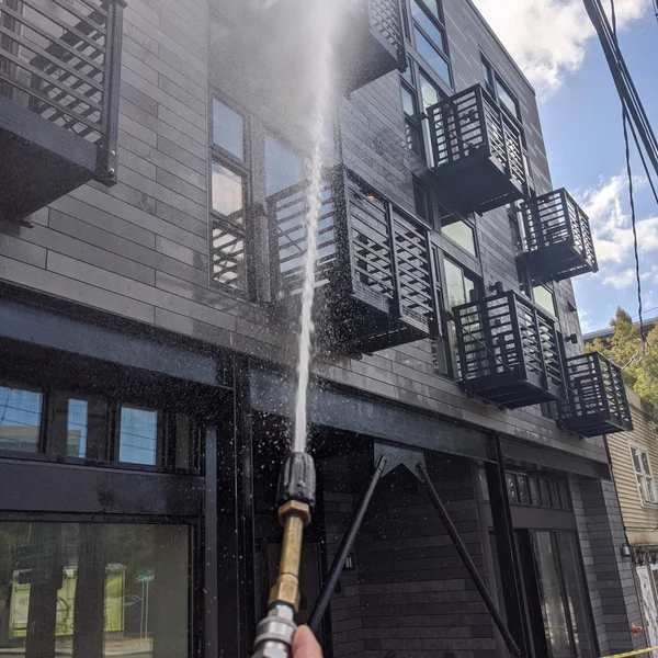 Pressure washing removes algae and moss from dark siding of a residential building for exterior maintenance.