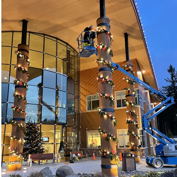 Technicians on a boom lift install commercial Christmas lights on building columns, part of exterior maintenance.