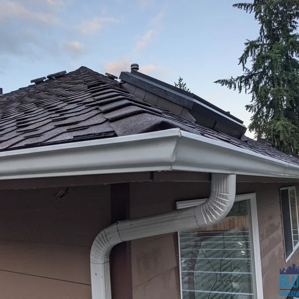 Clean white gutters and downspout on a brown house after professional gutter cleaning services.