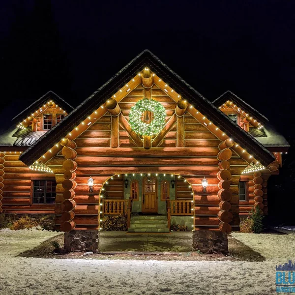 Log cabin home with professionally installed Christmas lights and a green wreath, showcasing exterior maintenance services.