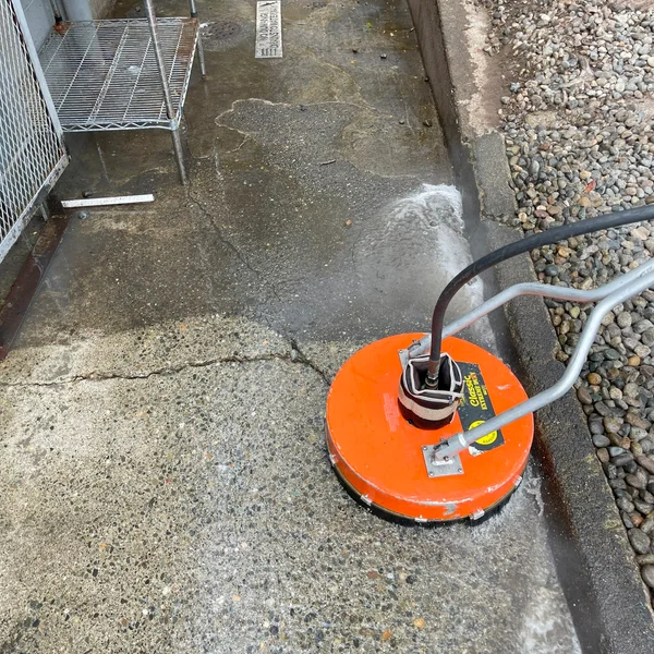 Orange surface cleaner being used to power wash a commercial concrete walkway for exterior maintenance.