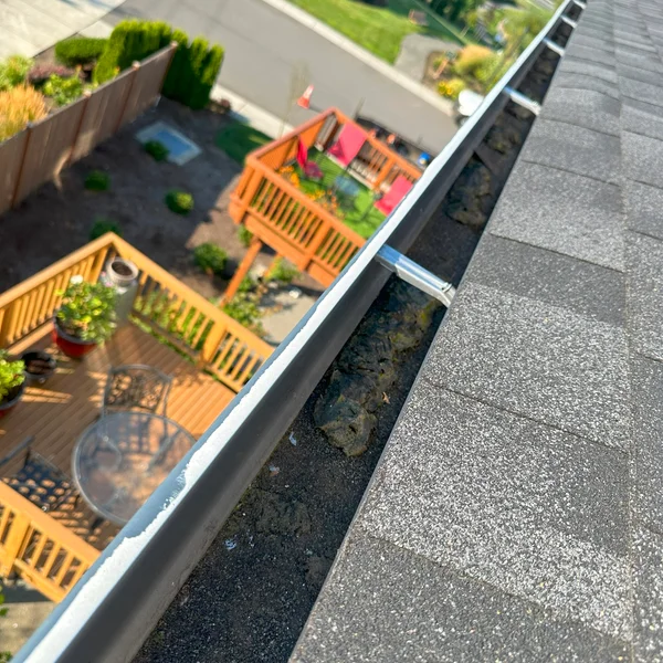 Gutters are clogged with dark debris on a gray shingle roof, a commercial gutter cleaning service issue.