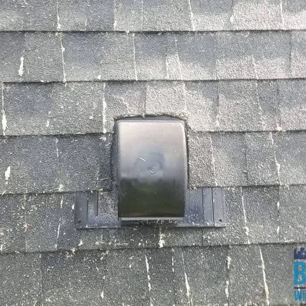 Dirty gray roof shingles surround a black roof vent; roof cleaning is needed.