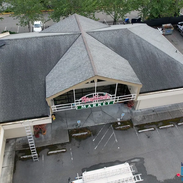 Commercial roof cleaning project on a market building shows gray shingles before soft wash service.