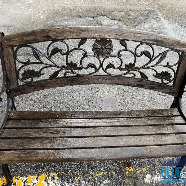 Wooden bench with decorative metal back, showing signs of weathering before residential wood restoration.