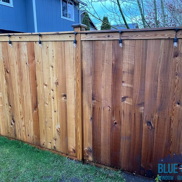 Restored wood fence shows before/after cleaning; half golden, half darker brown with string lights.
