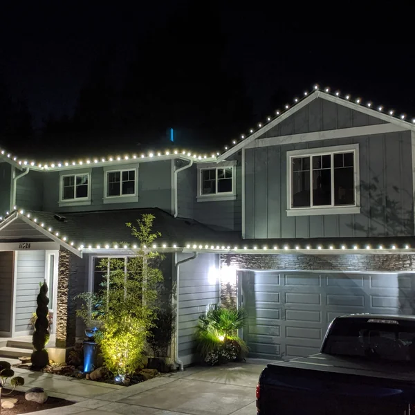 Gray two-story home is outlined with bright white Christmas lights by professional installers.