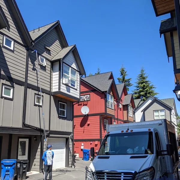 Residential gutter brightening service: technician cleans gutters using extension pole on a multi-unit building.