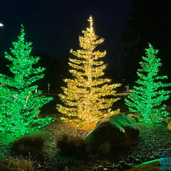 Commercial light installation features green and yellow Christmas trees near a rock.