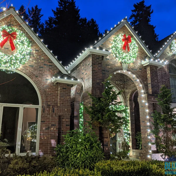 Brick home is decorated with Christmas lights, wreaths, and red bows by professional holiday lighting service.