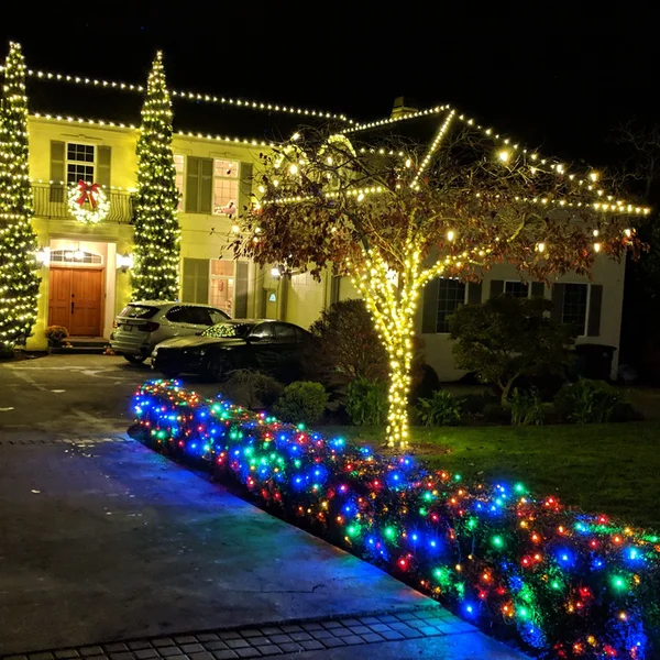 Residential Christmas lights illuminate a home's roofline, trees, and landscaping with colorful, festive decor.