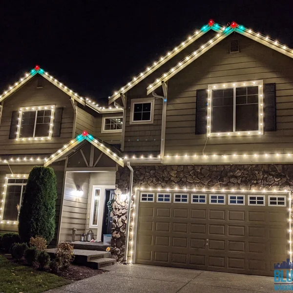 Residential house is decorated with warm white Christmas lights outlining roof and windows at night.