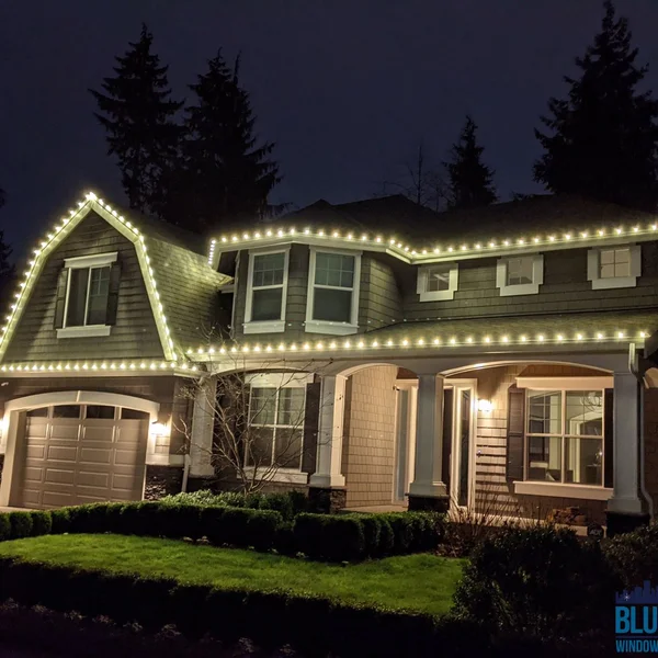 Residential house is illuminated with warm white Christmas lights installed by gutter cleaning and exterior maintenance