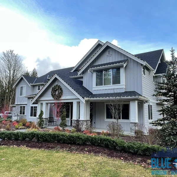 Gray two-story home with Christmas lights professionally installed on the roofline and a wreath on the front porch.