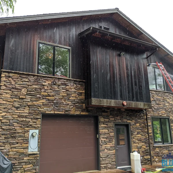 Residential wood and stone house shows roof and siding before professional algae and moss removal.