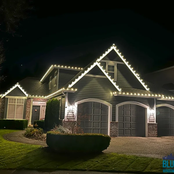 Residential house adorned with bright white Christmas lights along the roofline at night.