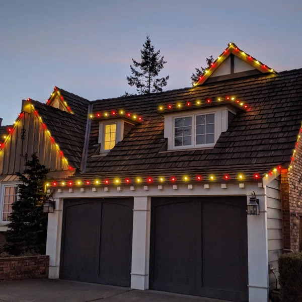 Red and yellow Christmas lights adorn a home's brown roof, showcasing professional residential holiday lighting installation.