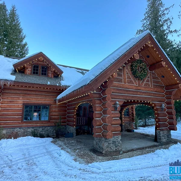 Log home's roofline is decorated with Christmas lights and topped with snow; gutter cleaning prevents winter damage.