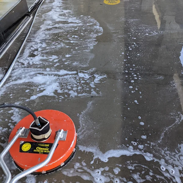 Commercial space concrete being cleaned with a surface cleaner, leaving a trail of white foam.