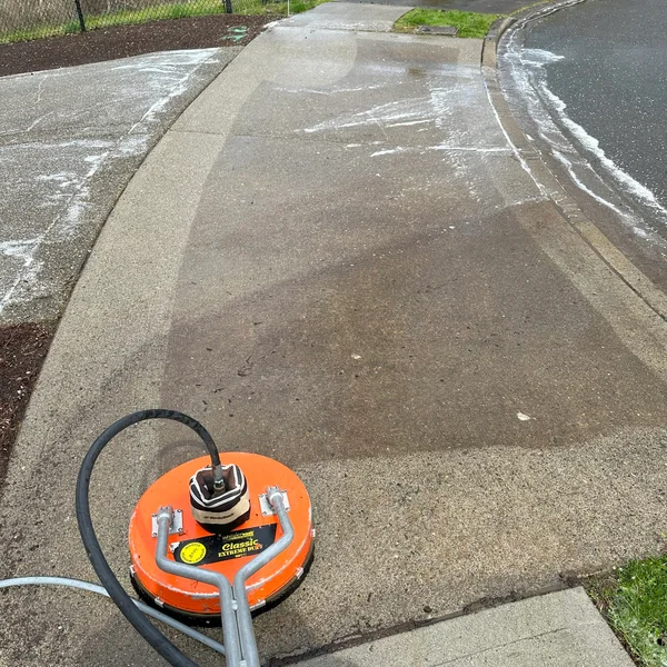 Concrete sidewalk and driveway being cleaned with an orange surface cleaner for professional pressure washing.