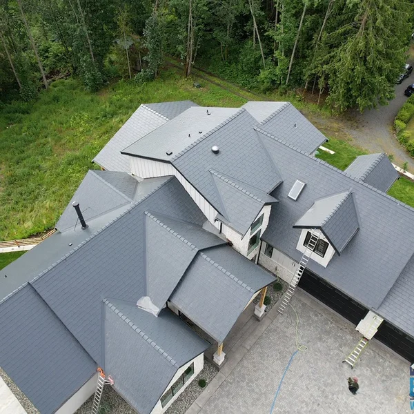 Residential roof cleaning results: Clean gray roof tiles on a house with light siding, set in a wooded area.
