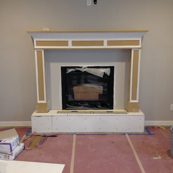 New fireplace construction in a home renovation project with white trim on a gray wall.