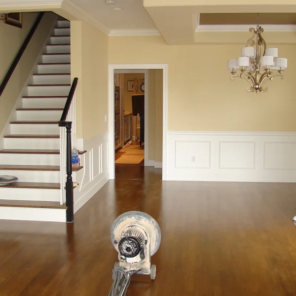 A Seattle home's brown hardwood floors are being refinished, showcasing the staircase, cream walls, and wainscoting.