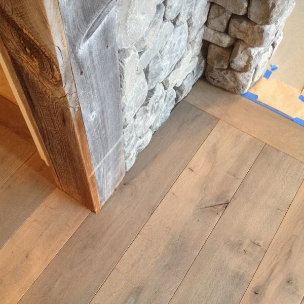 Close-up of light wood floors meeting a grey stone wall and weathered wood pillar in a remodeled Seattle home.