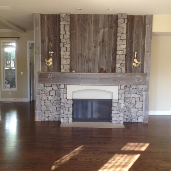 Seattle home renovation with stone fireplace and reclaimed wood mantle, flanked by sconces.