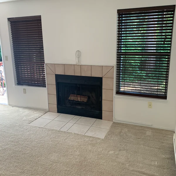 A Seattle home's interior shows a fireplace with beige tile surround, brown blinds on two windows, and neutral-colored