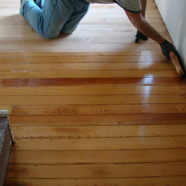 Seattle home renovation: A worker applies varnish to refinish light brown wood floors.