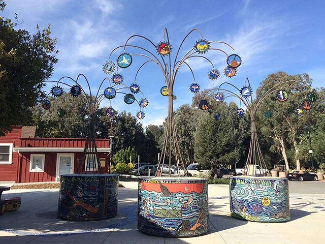 Mosaic-covered decorative trees create a whimsical community space near ADUs, Park Models, and Tiny Homes.