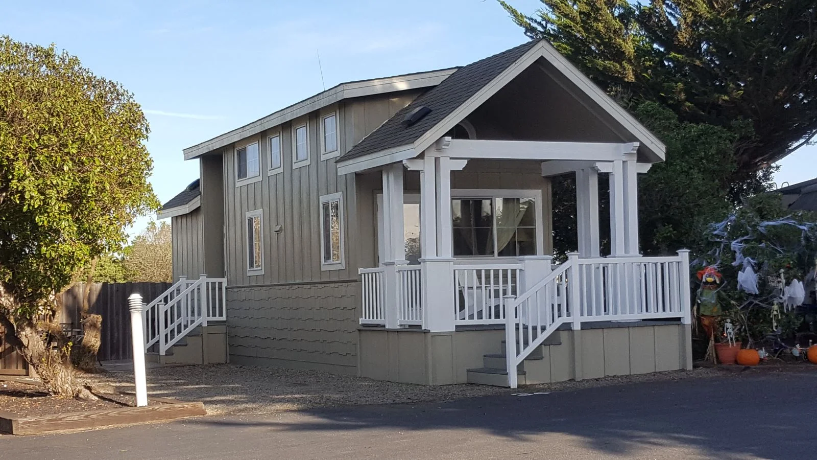 Exterior of a charming, sage green park model home with a welcoming white porch and railings.