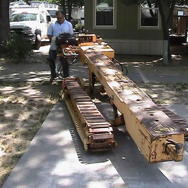 A man operates machinery for moving a park model tiny home on a paved surface near student housing.