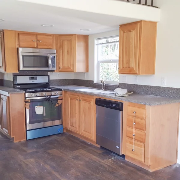 The kitchen of a manufactured home has wood cabinetry, a stainless steel range, and gray countertops.