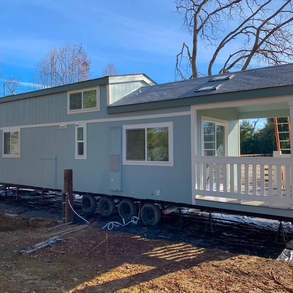 New blue park model home sits on a trailer, ready for placement in a residential or vacation setting.