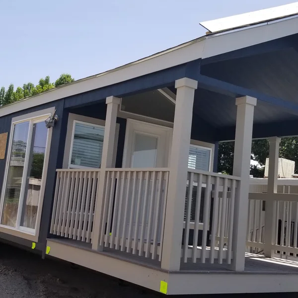 This modern park model home features durable navy blue siding, elegant white columns, and a covered front porch perfect for outdoor relaxation.