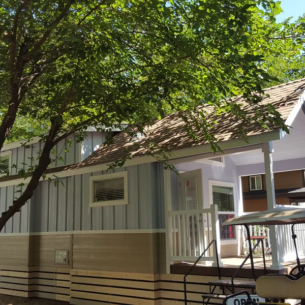 This beautifully designed park model tiny home features a spacious front porch, vertical blue siding, and durable wood-look skirting, perfect for a cozy backyard ADU.