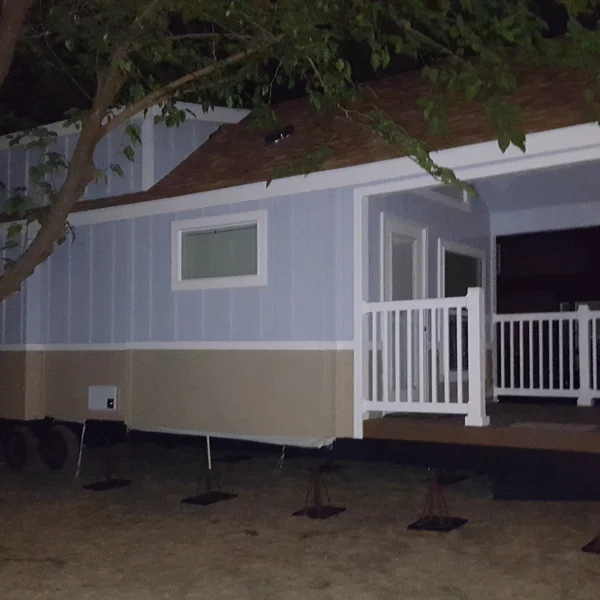 This custom park model tiny home on wheels features a two-tone blue and tan exterior with a covered front porch, perfect for an ADU.