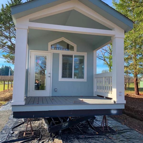 A light blue park model home with a white porch awaits installation.