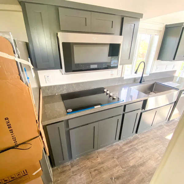 Modern tiny home kitchen features gray cabinetry, stainless steel appliances, and a farmhouse sink.