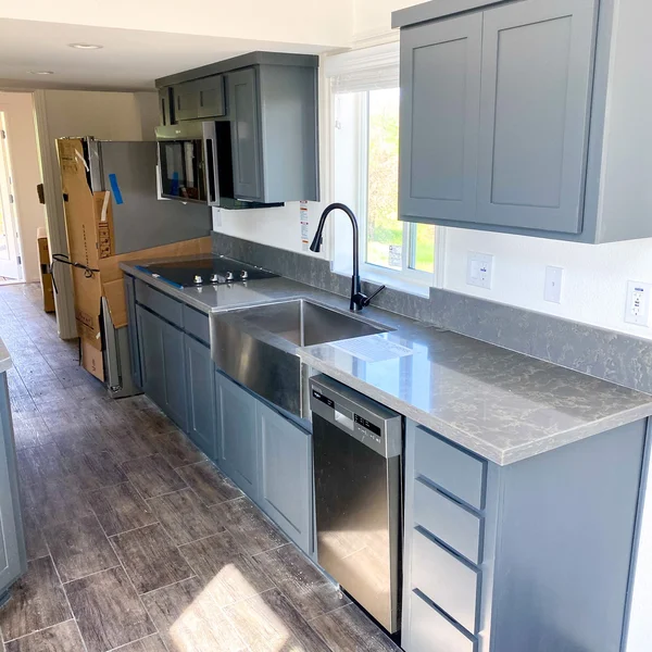 Newly installed kitchen in a manufactured home features gray cabinets, stainless steel appliances, and wood-look tile