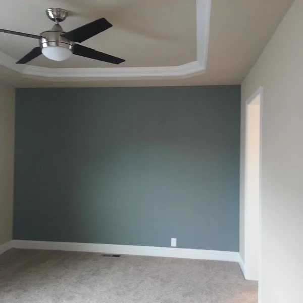 A bedroom with light beige carpet and a dark teal accent wall inside a manufactured home.