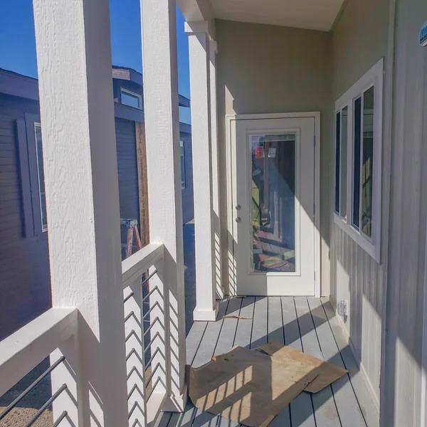 Covered porch with white pillars and railing leads to the entrance of a newly constructed manufactured home.