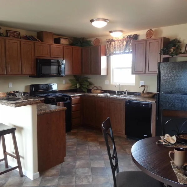 A well-lit manufactured home kitchen features wood cabinets, black appliances, and a cozy dining area.