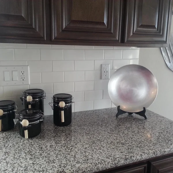 Interior kitchen shows black canisters and silver decorative plate atop speckled granite counters in a manufactured home.