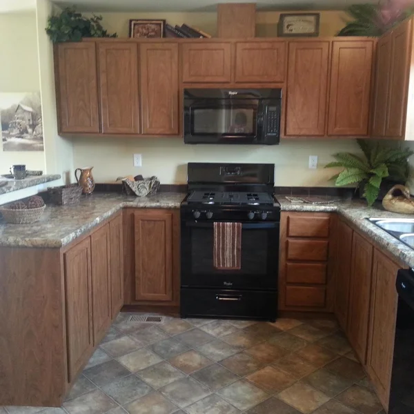 This manufactured home kitchen features wood cabinets, black appliances, and tile flooring for a cozy feel.
