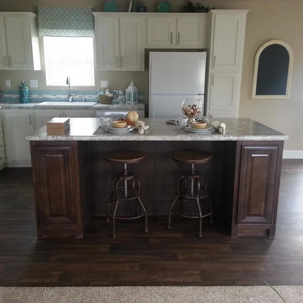 Modern manufactured home kitchen features white cabinets, a granite-topped island, and vintage-style metal bar stools.